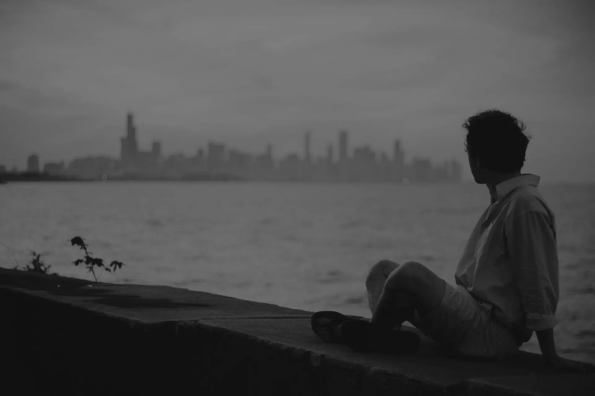 A man sitting by the water looking at a city skyline